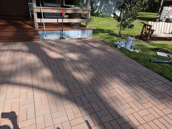 The finished brick paver patio, flat and clean, beside a wood deck
